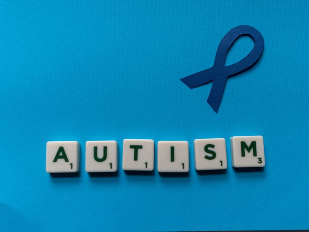 A blue ribbon to symbolise neurodiversity with scrabble letters underneath, which spell out autism.