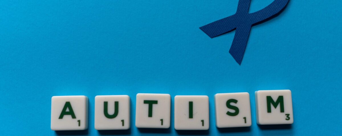 A blue ribbon to symbolise neurodiversity with scrabble letters underneath, which spell out autism.