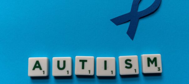 A blue ribbon to symbolise neurodiversity with scrabble letters underneath, which spell out autism.