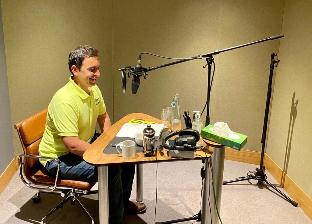 Steven Mifsud sat inside a recording booth recording from a script.