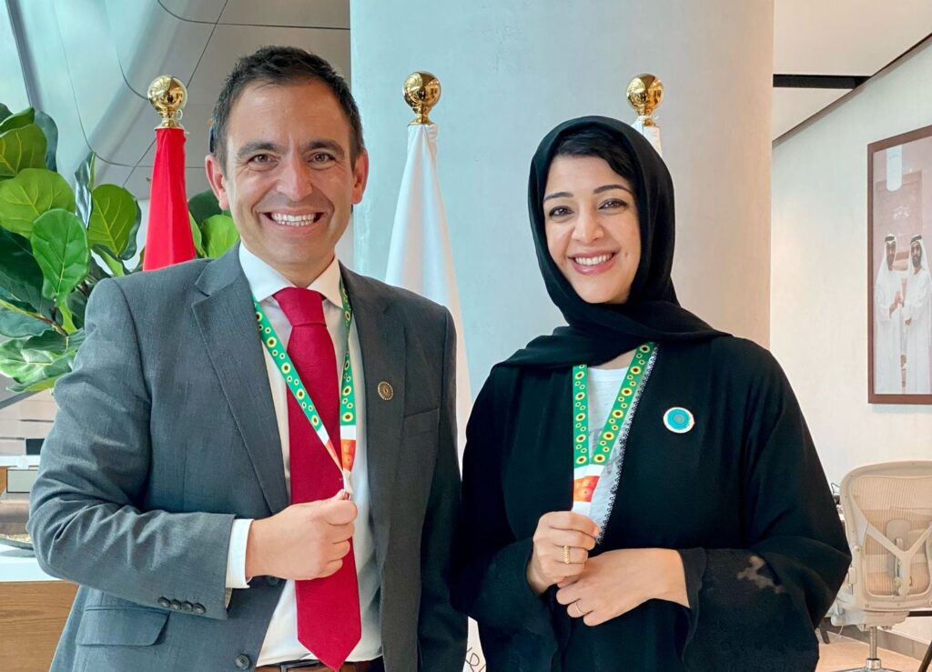 A portrait photo of Steven Mifsud MBE with Her Excellency, Reem Al Hashemy wearing hidden disability sunflower lanyards.