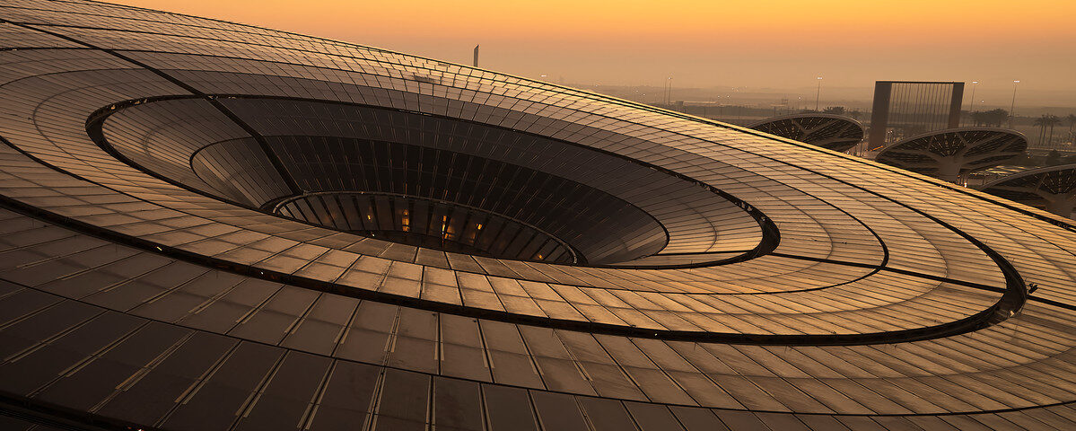 A birds eye view of the Sustainability pavilion at Expo 2020 Dubai during sunset, a large, slanted, disc shaped building.