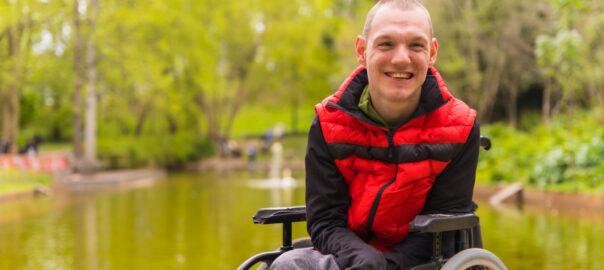 Young male wheelchair user next to a pond in a public park.