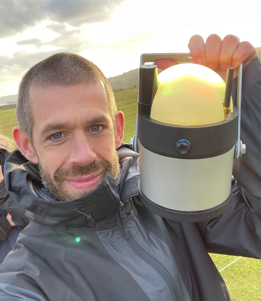 Direct Access Consultant Jamie standing in a field holds up an electronic lantern and smiles for a selfie.