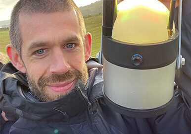 A photograph of Access Consultant Jamie Rhys-Martin holding an electric lantern in a field during the Green Space, Dark Skies event.