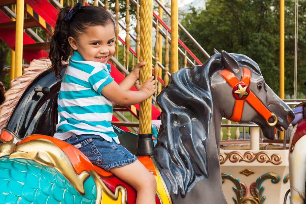 A small female child rides a horse on a carousel smiling at the camera.