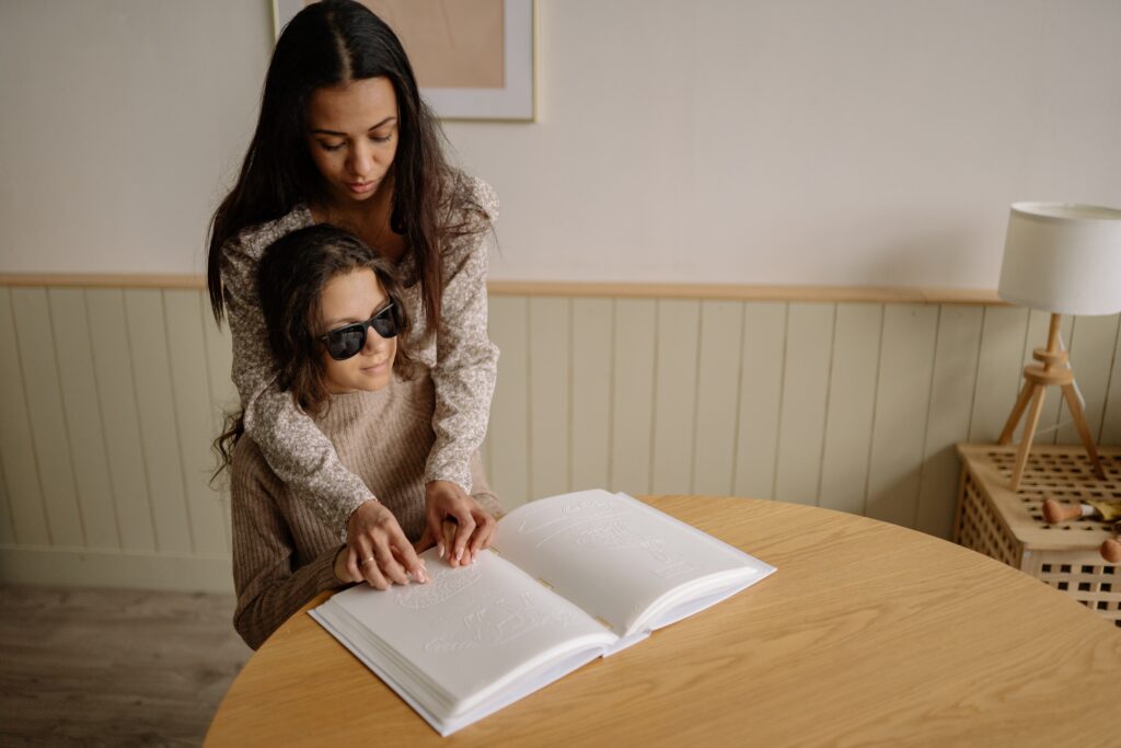 A young woman helps a female blind child interpret the image of a hedgehog in a braille book.