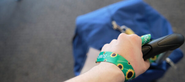 Hand of an unrecognizable person dragging a suitcase, wearing on the wrist a lanyard of sunflowers, symbol of people with invisible or hidden disabilities.