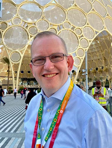 A dark blue graphic showing a photograph of a smiling Steve Dering, a middle aged Caucasian man with short brown hair. He is wearing a blue shirt with a green sunflower lanyard around his neck.