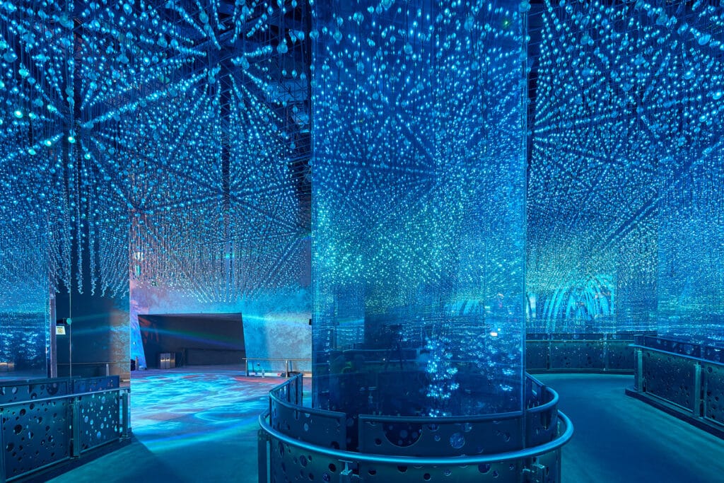 General view of the Under the Sea exhibition as part of Terra The Sustainability pavilion at Expo 2020 Dubai. A large room with exhibits lit by sea blue fairy lights designed to mimic underwater views illuminates the exhibits.
