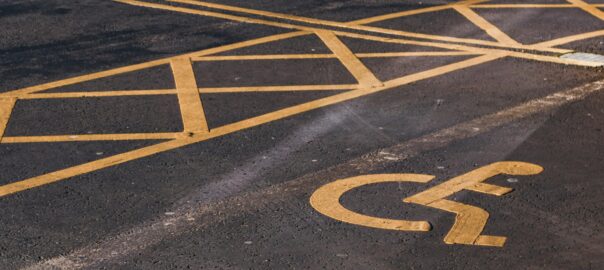 An accessible parking bay with the international symbol of access (person in a wheelchair) painted on the tarmac in yellow.