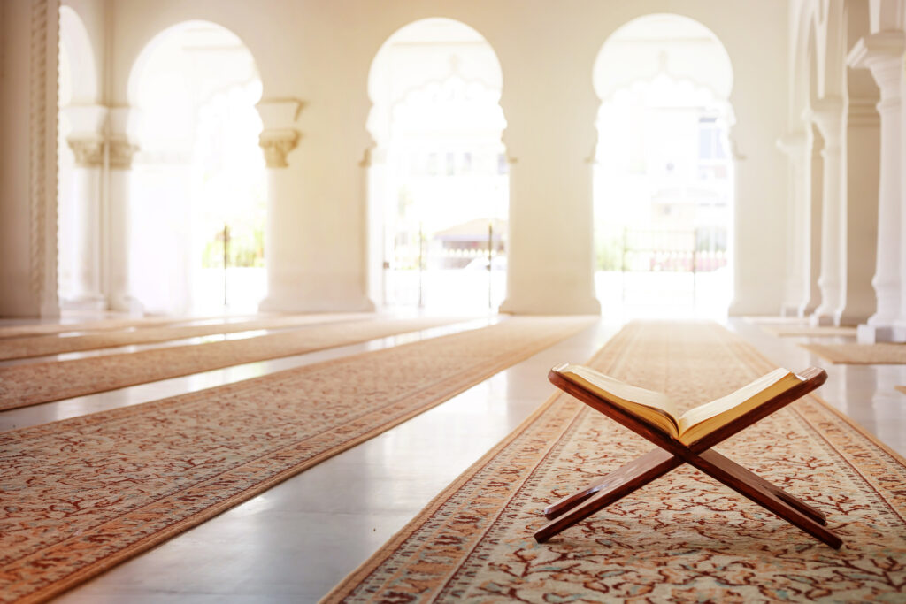 A general view of an empty Mosque interior during the day. In the foreground of the photo is a copy of the Quran, the holy book of Islam left open on a small wooden support device.