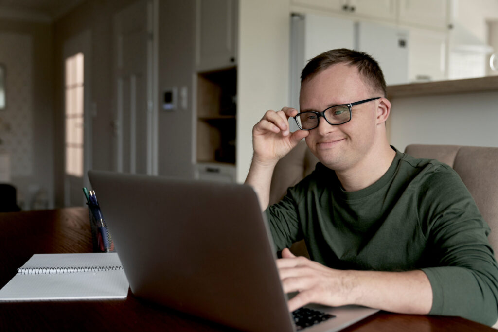 Cheerful adult man with down syndrome using laptop at home.
