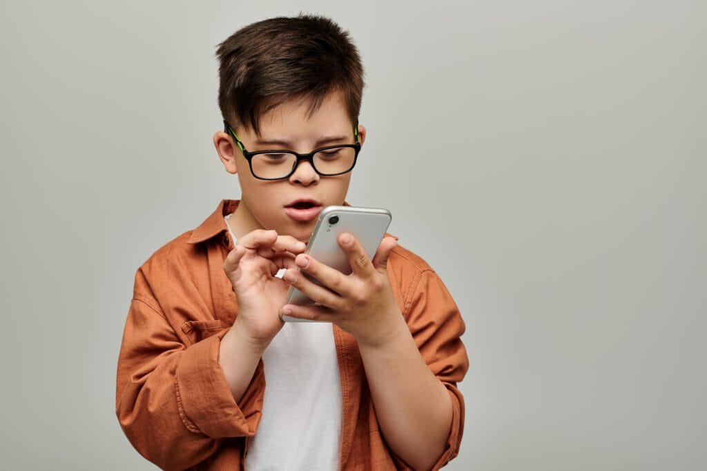 A little boy with down syndrome wearing glasses focuses intently on a mobile phone, scrolling on the screen.
