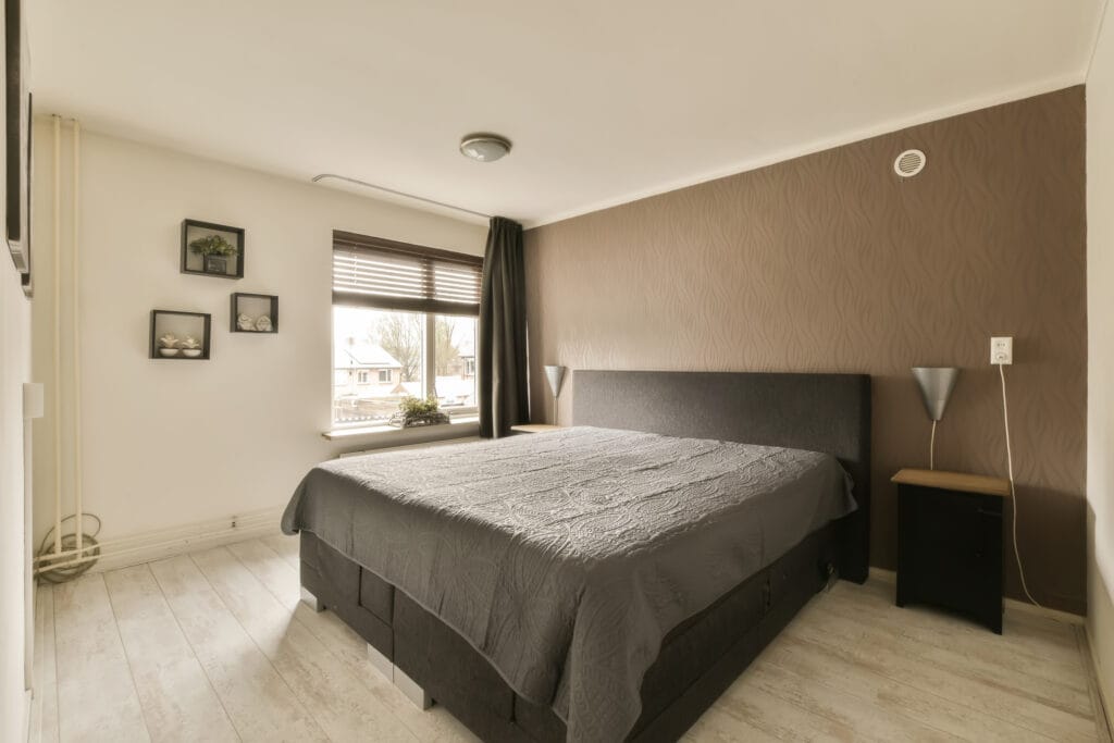 A bedroom with brown walls and white flooring, there is a large bed in the room has a black headboard on it.