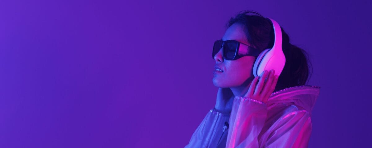 Beautiful,Woman,With,Purple,Hair,In,Futuristic,Costume,Over,Dark A pretty young woman wearing dark glasses and headphones in a sensory room, which is lit up purple.
