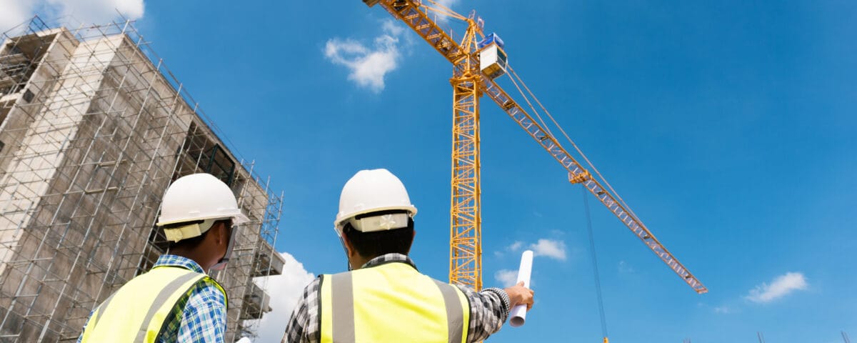Construction,Engineers,Discussion,With,Architects,At,Construction,Site,Or,Building Two male engineers wearing hi-vis jackets and white hard hats have a discussion on a building site on a sunny day.