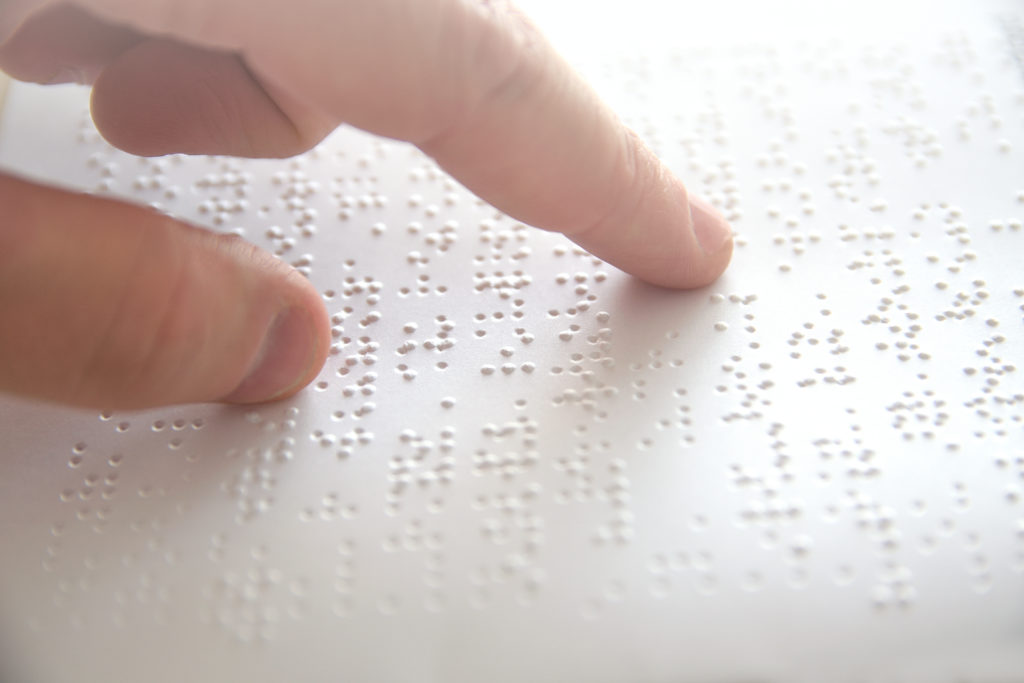 A close-up shot of a persons finger reading Braille paper.