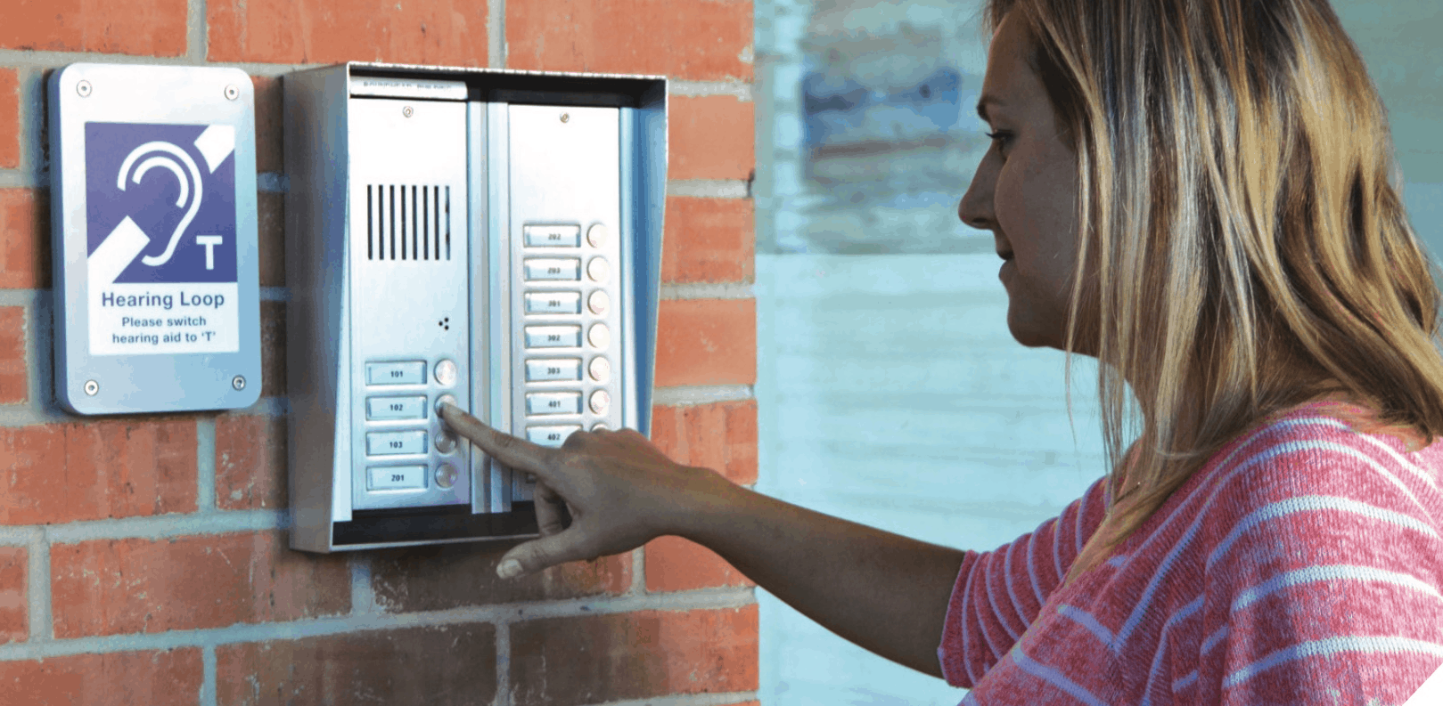 Young lady pressing a button on an Intercom Hearing Loop outside a building.