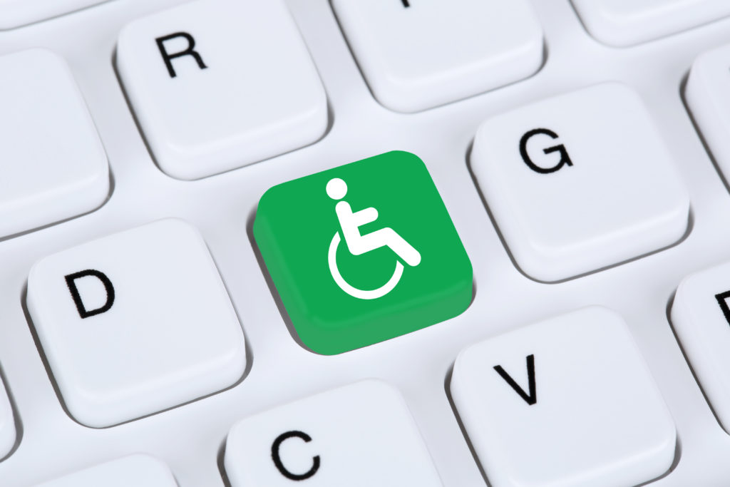 A close up on a white computer keyboard with one green keypad showing the international symbol of access (a symbol of a wheelchair).