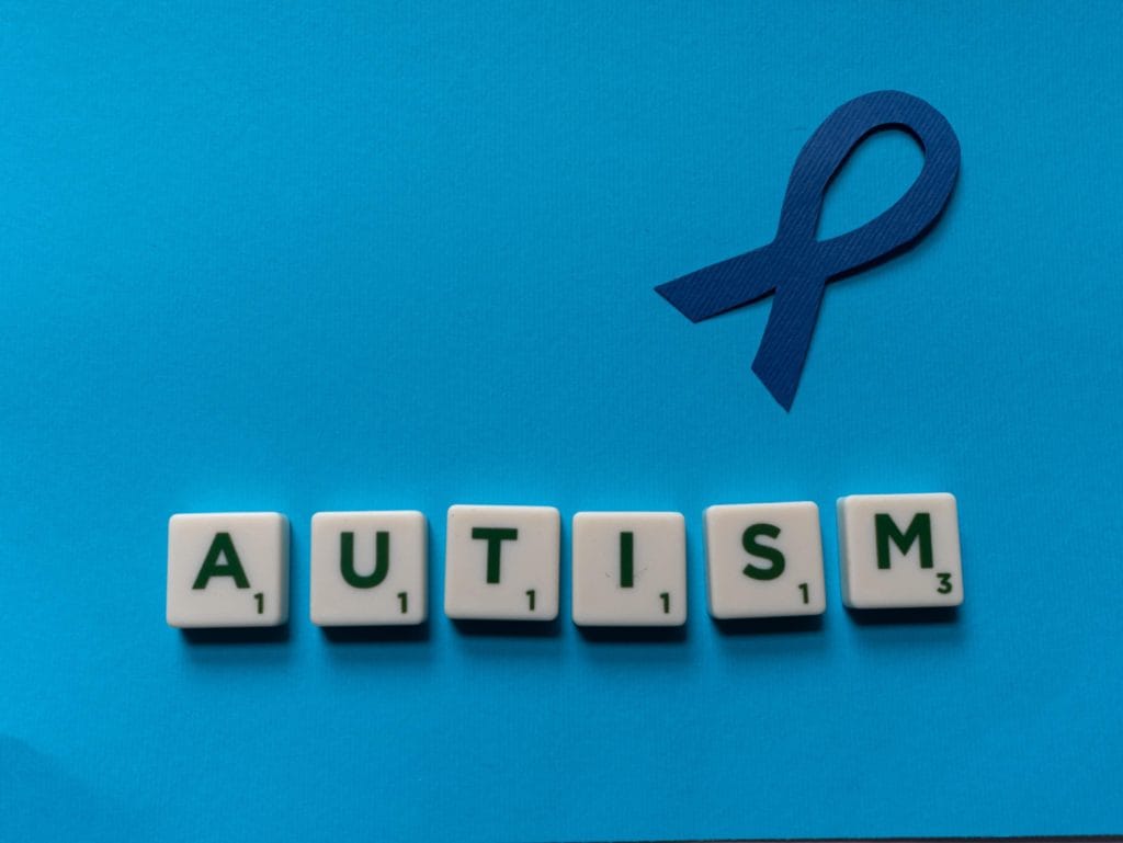 A blue ribbon to symbolise neurodiversity with scrabble letters underneath, which spell out autism.