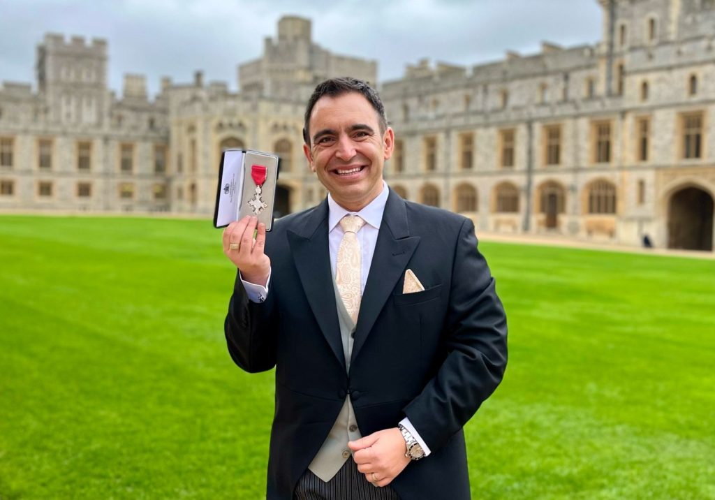 Steven Mifsud holding his MBE medal on the grounds of Windsor Castle on an overcast morning.