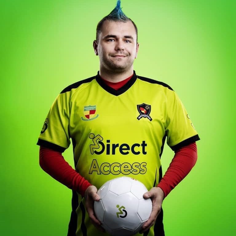 Nantwich Town Wolves VIFC captain Craig Acton holding a football with both hands against a green backdrop. His kit features the Direct Access logo.