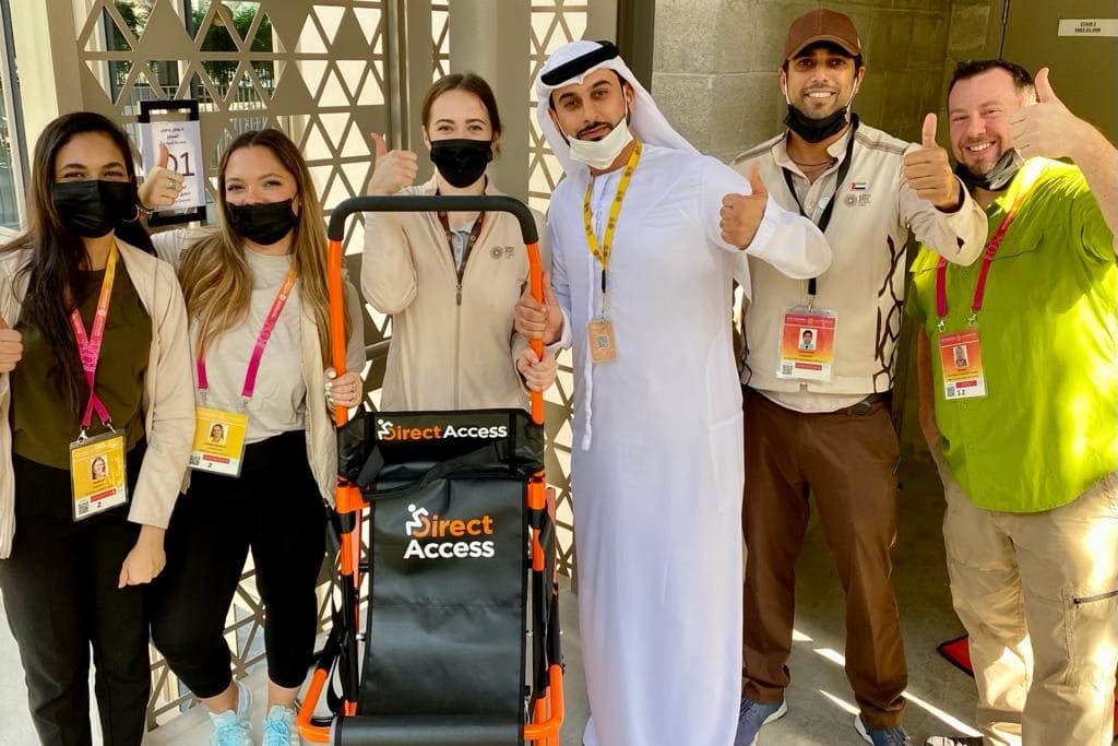 A mixed group of students with their thumbs up next to a Direct Access Evacuation Chair