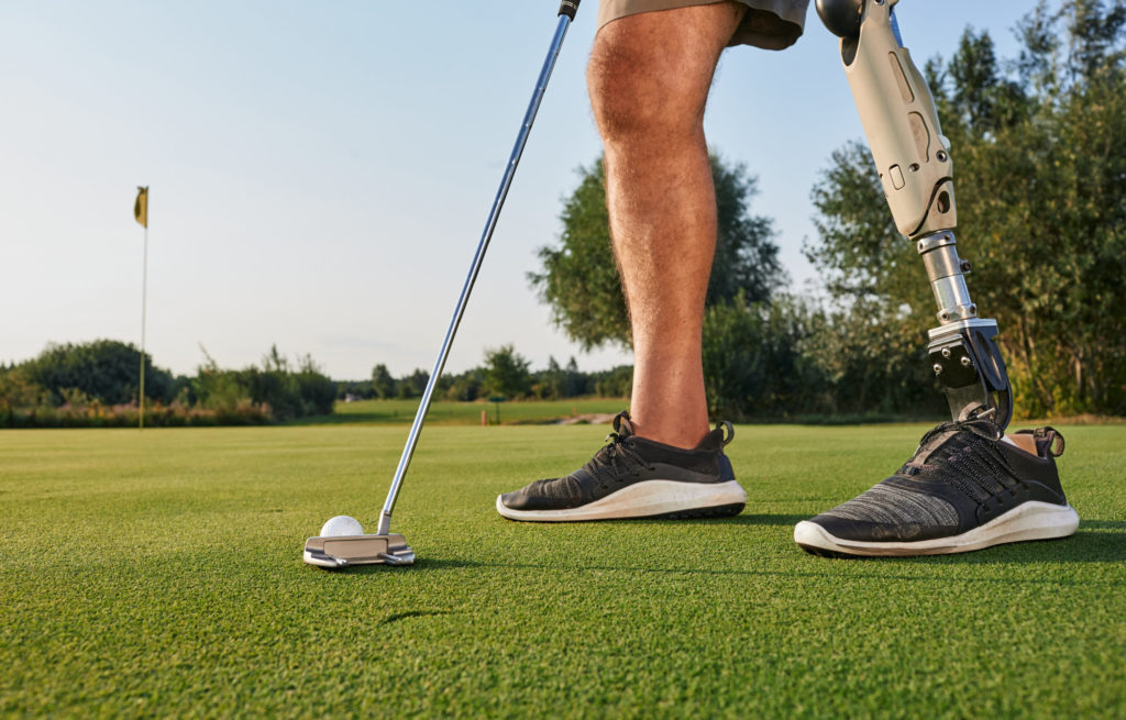 Professional golfer with prosthetic leg hitting a golf ball with a putter on a sunny day