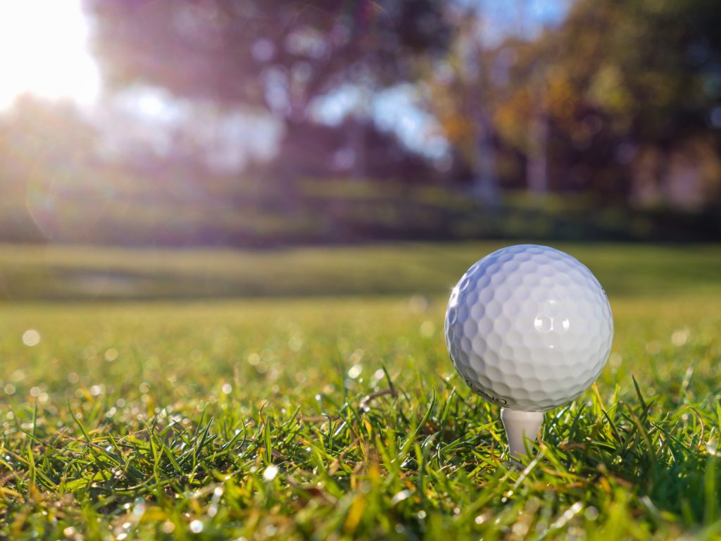 Golf ball on a tee with a sunlit green in the background