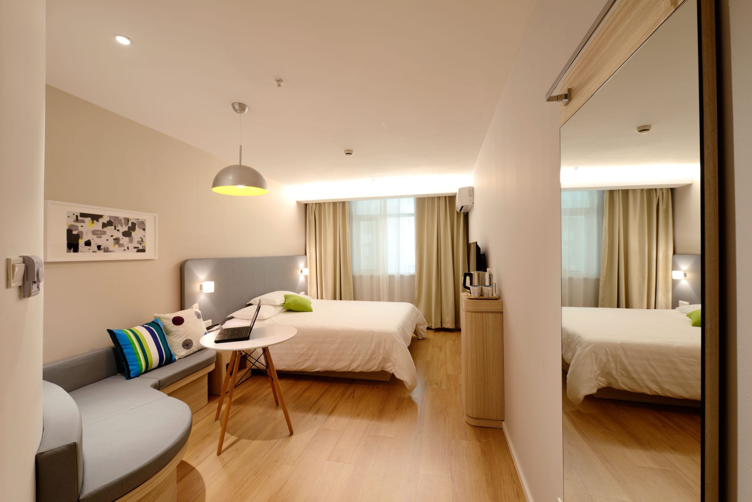 Brightly lit hotel room with a bed, white table aside it, and mirror wall