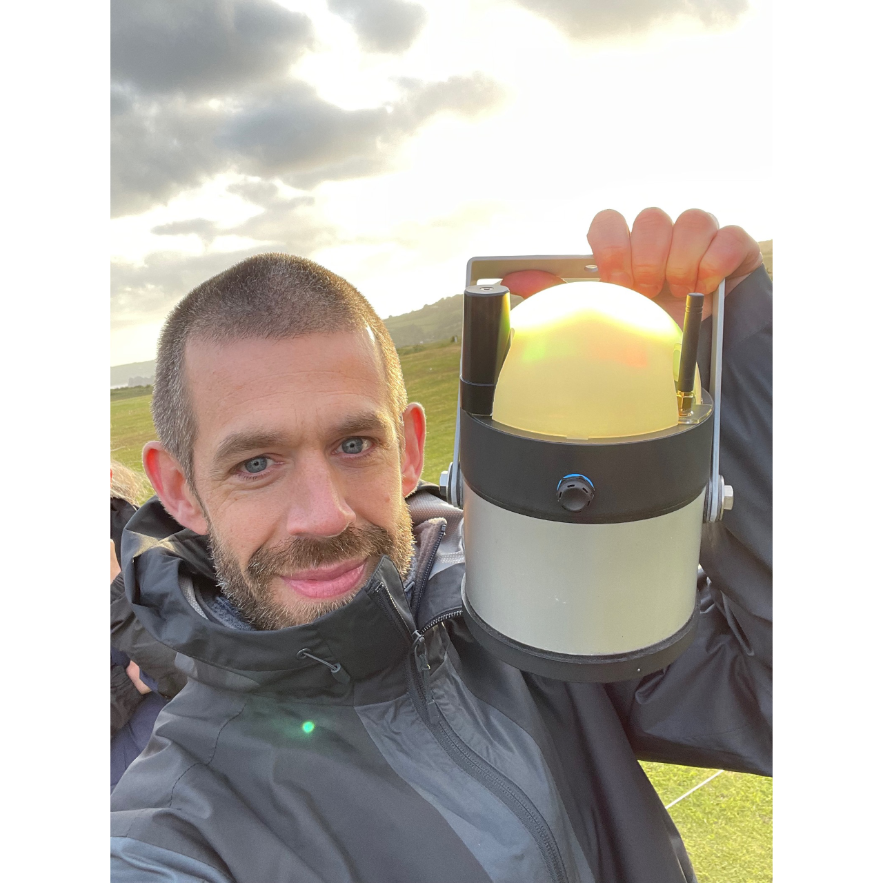 Direct Access Consultant Jamie standing in a field holds up an electronic lantern and smiles for a selfie