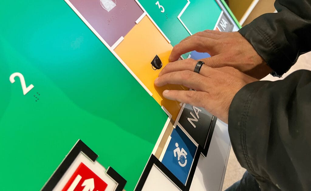 Close up of a man's fingers interpreting a Direct Access braille map board for a museum. Specifically, an image of a tea cup, insinuating the location of an on-site cafe.