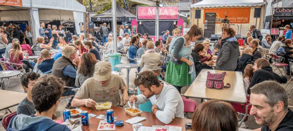 Group of people on benches eating food and socialising at Nantwich Food Festival.