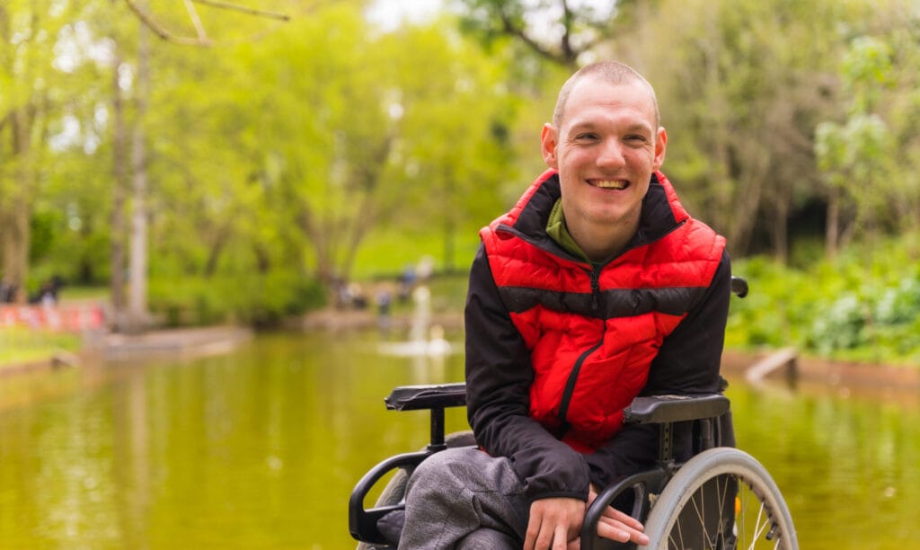 Young male wheelchair user next to a pond in a public park.