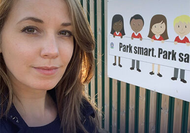 A photograph of Education Access Consultant Sophie Malton posing for a selfie outside a school. A sign which reads "Park smart. Park safe" is on the wall behind her.