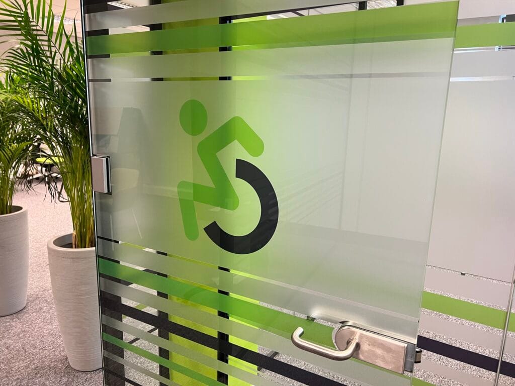 A photo of a glass door with Direct Access signature wheelchair logo as its manifestation.