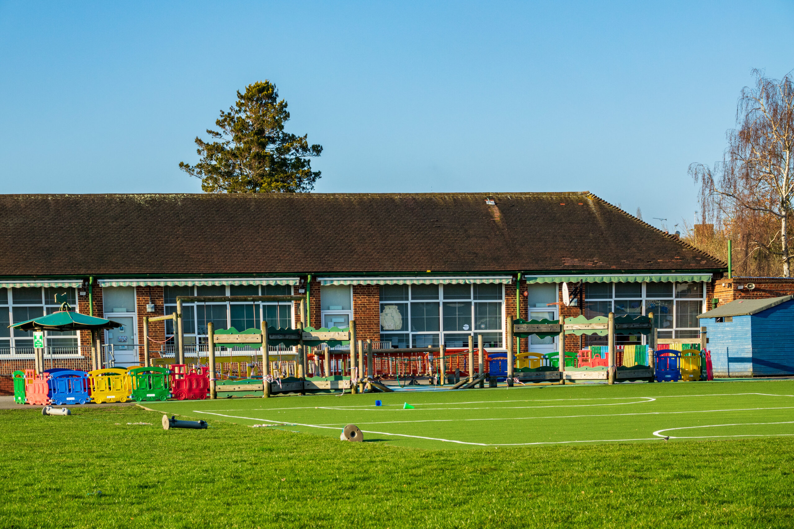 A British Junior school playground outside an infant school with a small football field and various outdoor toys and climbing amenities.