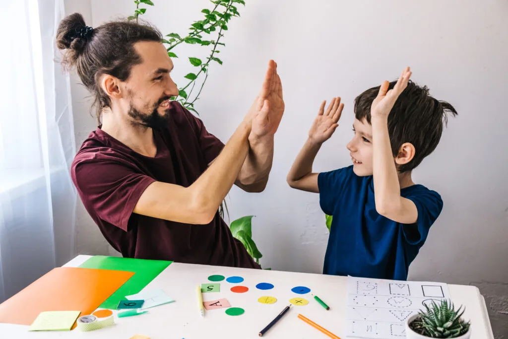 A happy autistic boy high fiving his school tutor, learning and having fun together.