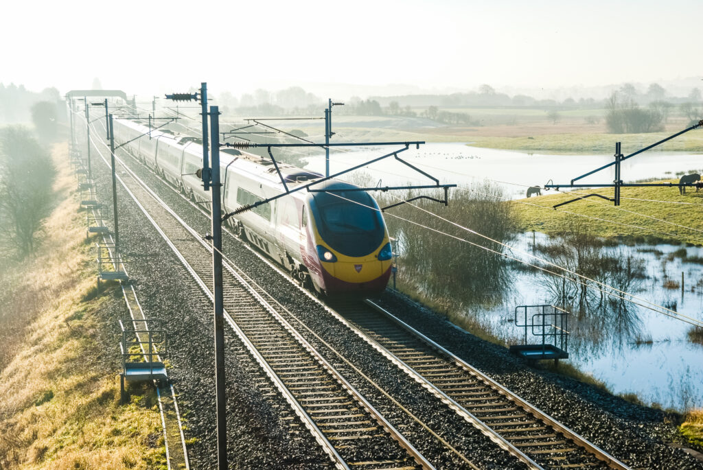 A Virgin Train Express passenger train races across a track in the countryside.