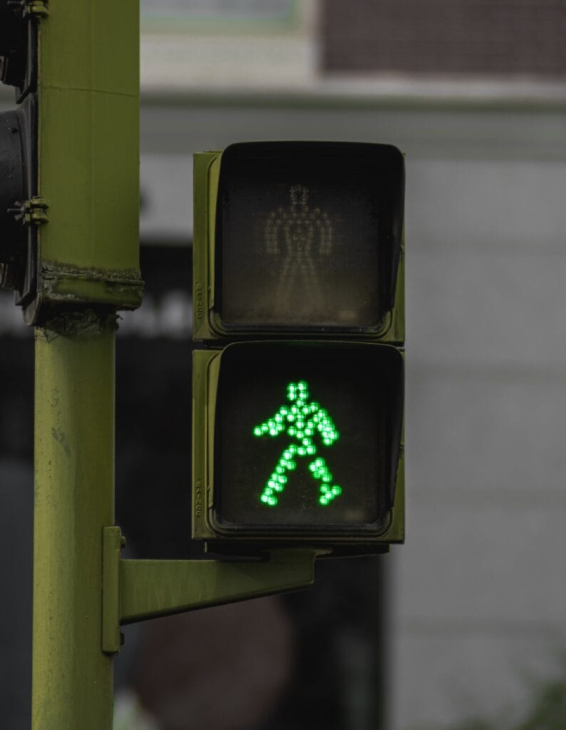 A photograph of a green man sign on a green pole.