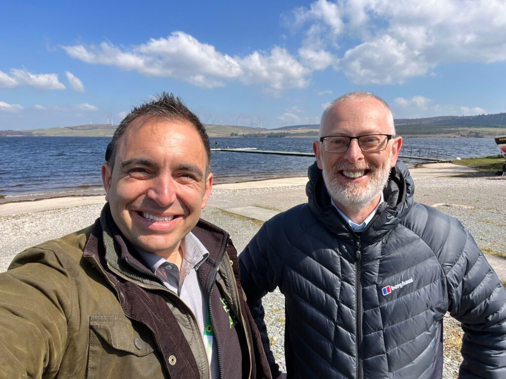 A selfie photograph of Steven Mifsud (Direct Access CEO) and Jamie Watson (Access Consultant) smiling with a lake and pier in the background on a cloudy day.
