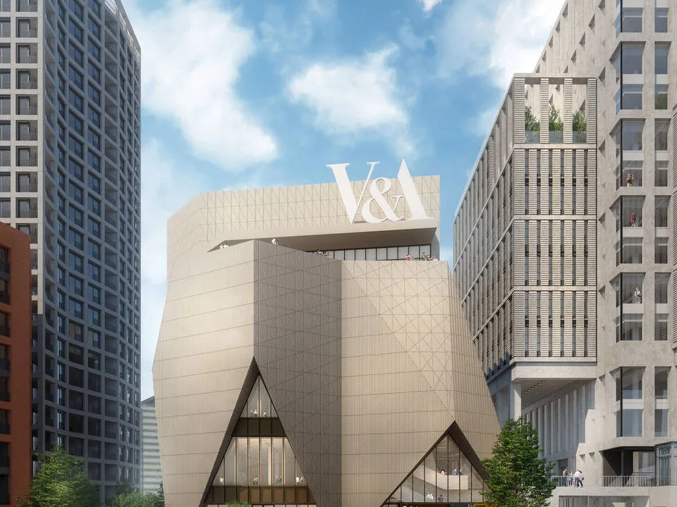A proof of concept photo of the V and A East museum, showing a large, baige building that looks like an upside down crown. A large V and A sits on the top. Outside crowds of people commute on the open plan path space. At the forefront, a set of stairs lead down to a nearby canal with a red, white, and blue coloured boat passing by.