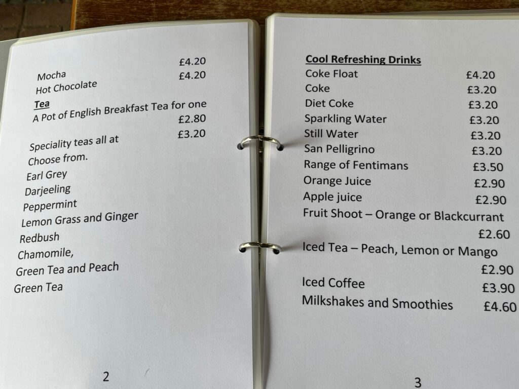An open folder with a simplified, large print accessible menu inside listing a selection of teas and cool refreshing drinks.