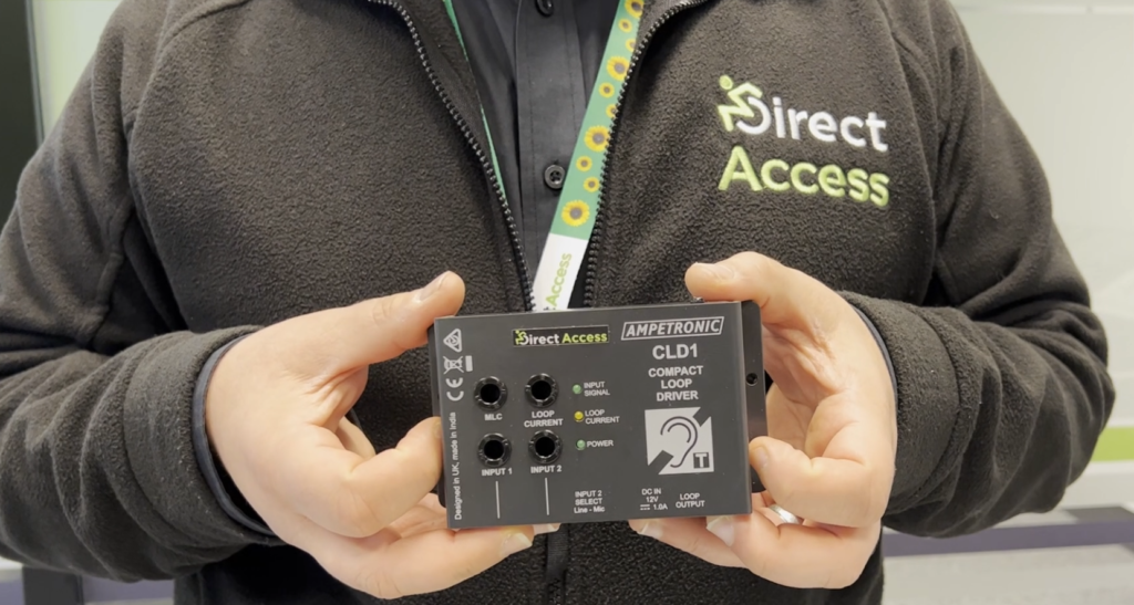 A man wearing a hidden disability sunflower lanyard holds up a black, rectangular counter induction loop in both hands.