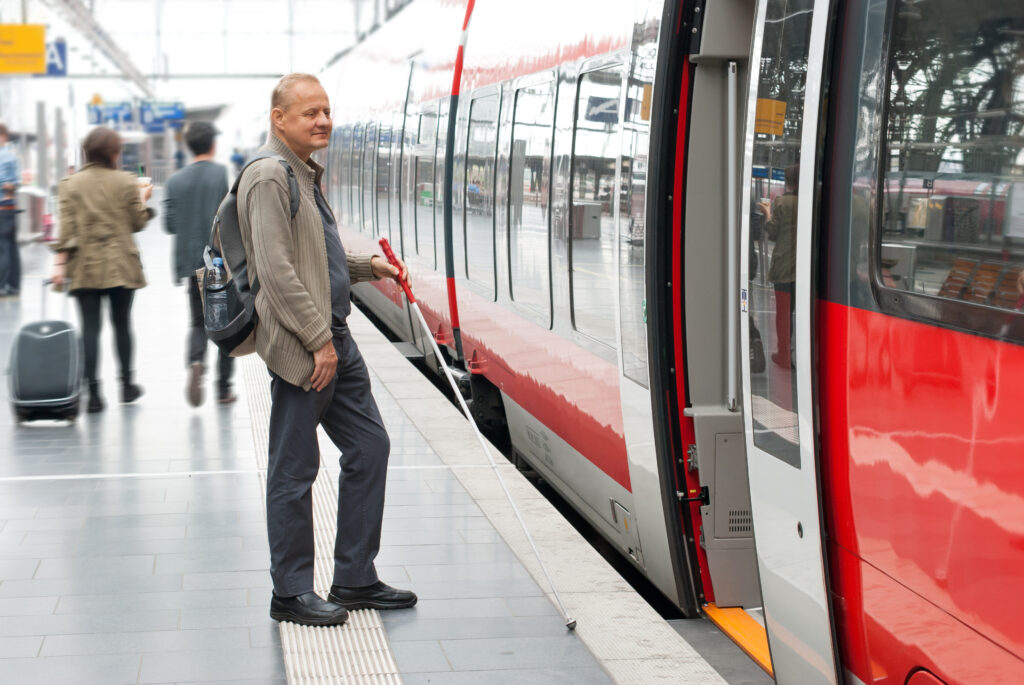 A visually impaired man boards a train at a station.