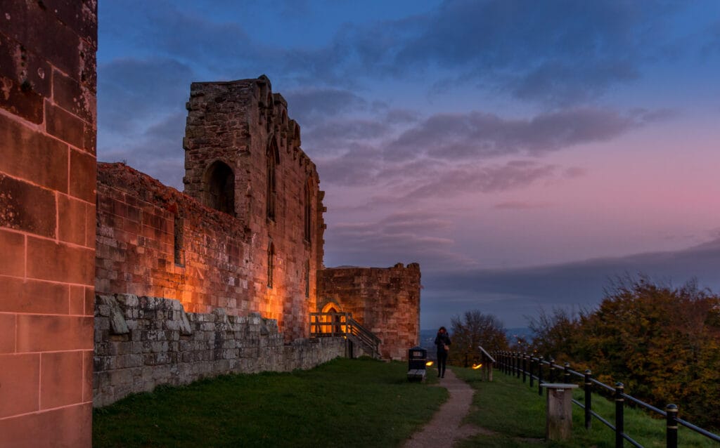 A beautiful sunset reflects on the ancient Stafford Castle. Underhead lighting gives the brick walls of the castle a blood orange look The colourful sky in the background is a mixture of blue and pink as the sun sets.