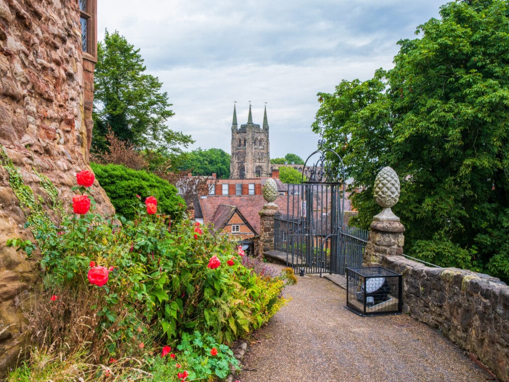 The view of St Editha's church from the entrance to Tamworth Castle, UK. A beautiful mixture of red flowers overflow slightly onto a stone pavement leading towards the church.