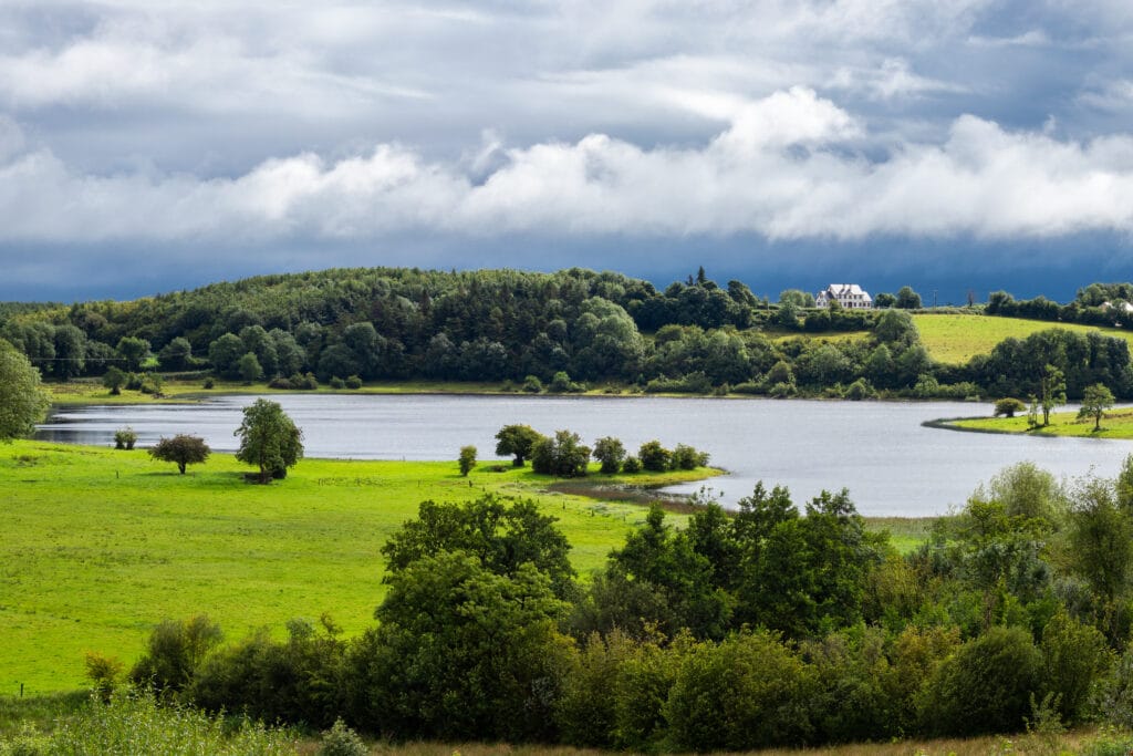 Stormy clouds in the afternoon hover over a field in Cavan, County Cavan, Ireland. A white house can be seen in the distance.