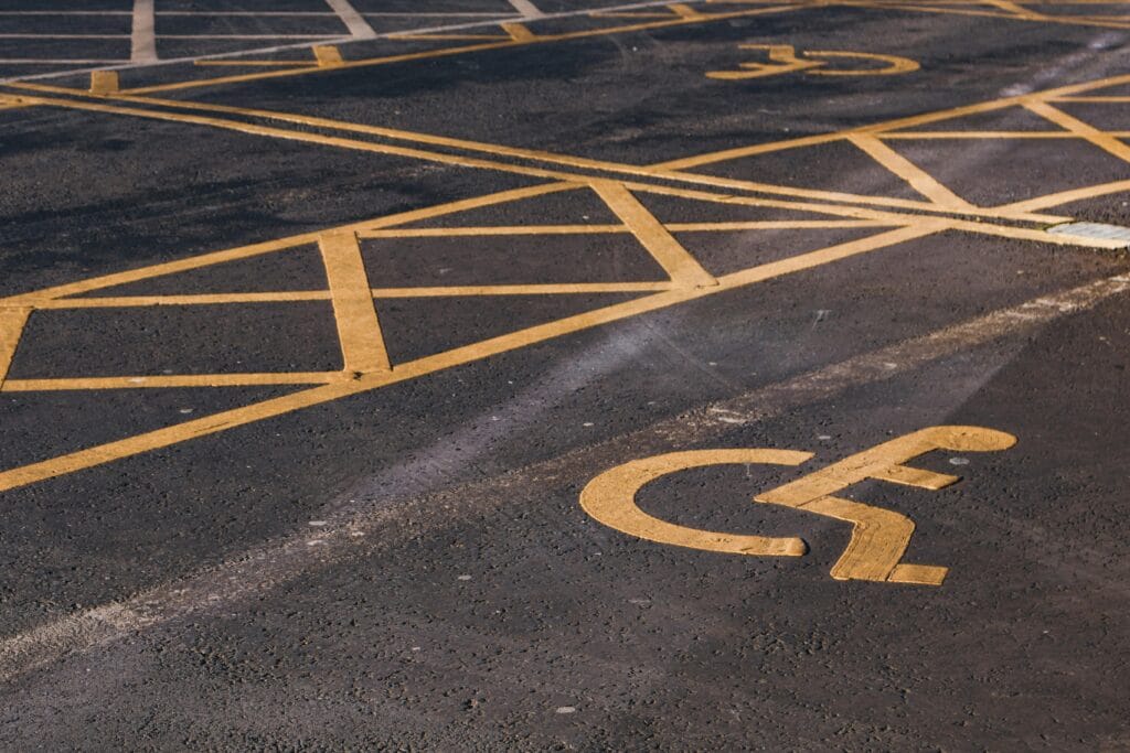 An accessible parking bay with the international symbol of access (person in a wheelchair) painted on the tarmac in yellow.